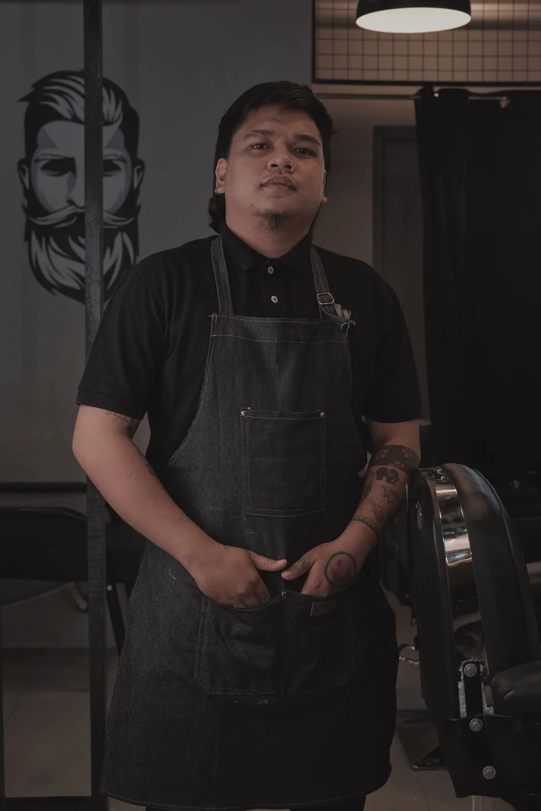 A barber in a denim apron beside his chair