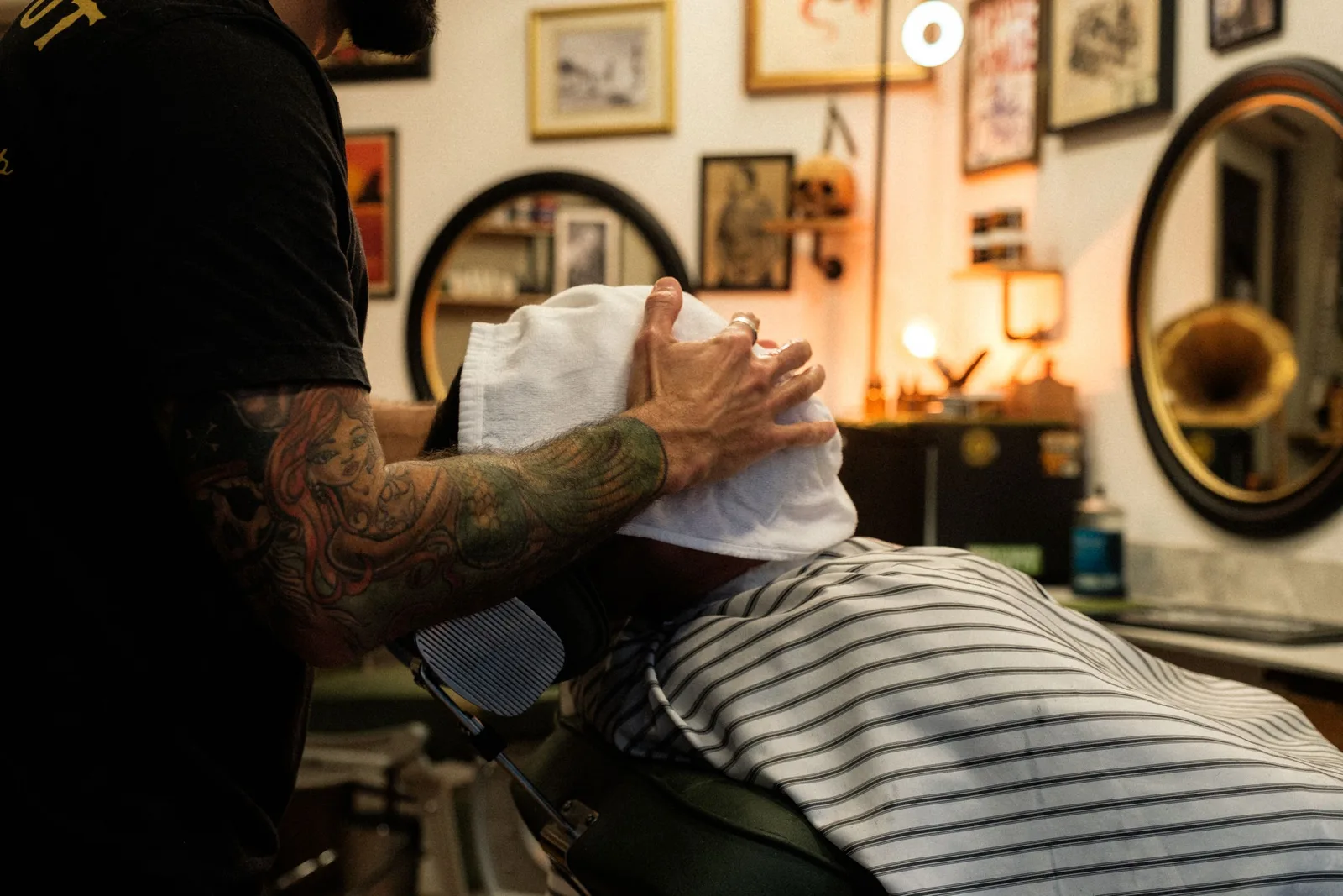 A barber pressing a hot towel onto a reclined client’s face