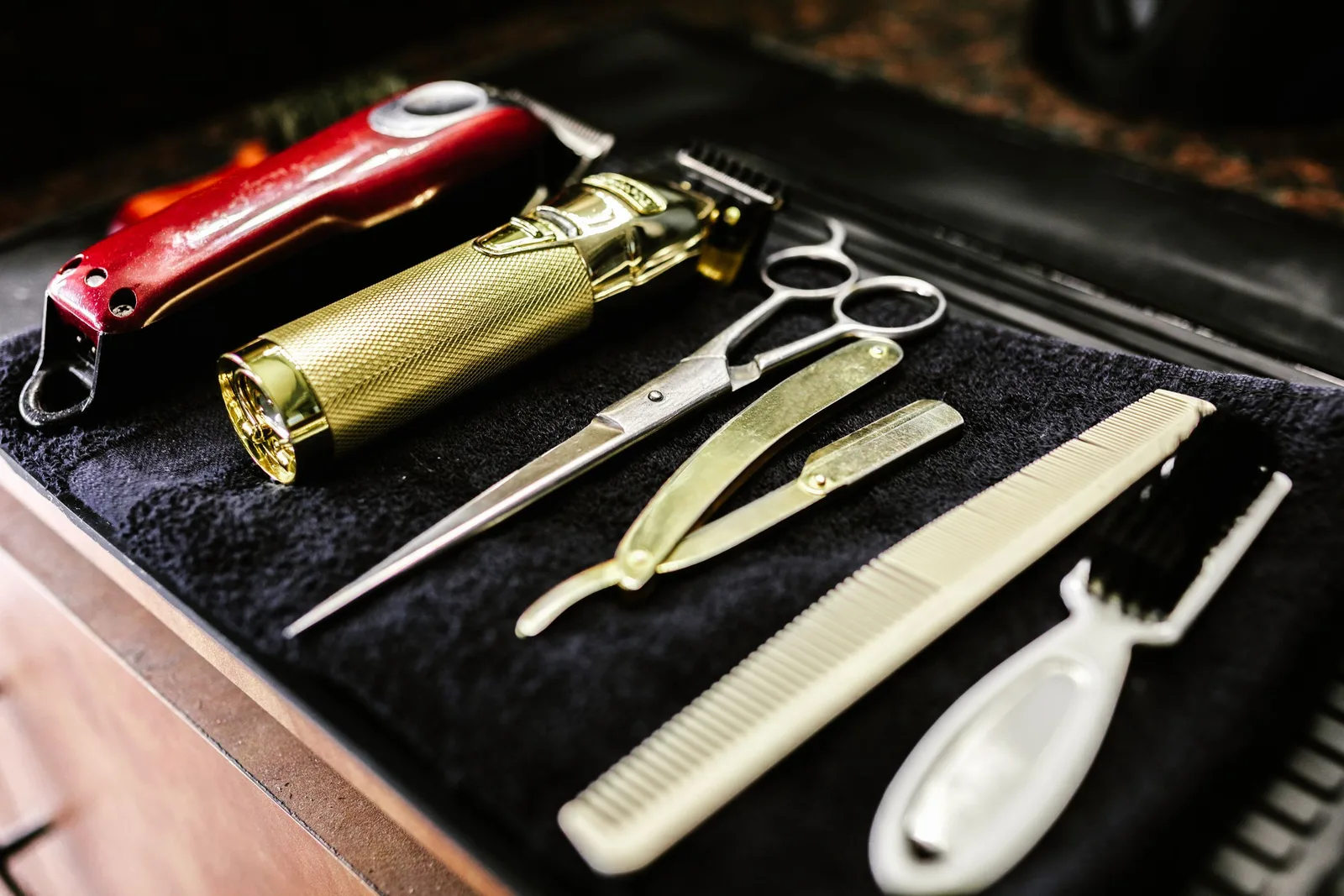 Clippers, scissors, a razor and a comb on a black towel