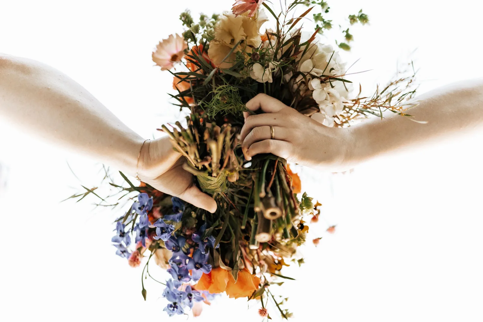 Two hands holding a mixed bouquet of dried and fresh flowers against a white background