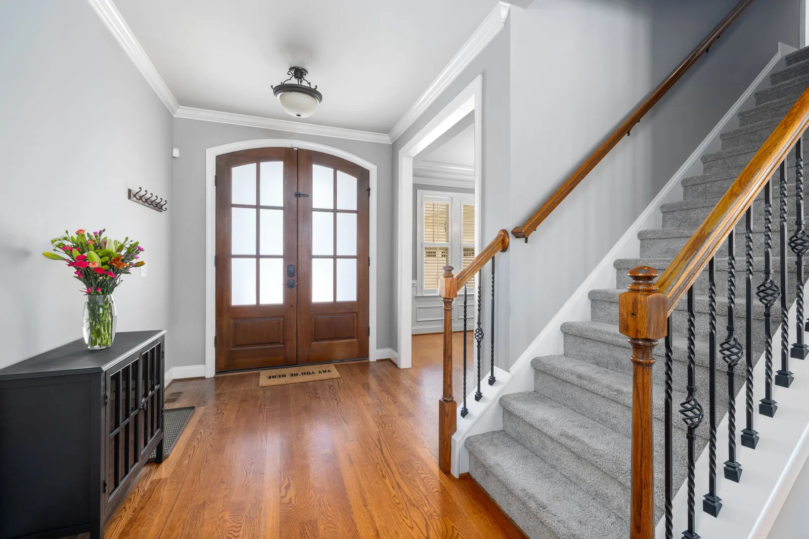 A home entry hall with a wooden double front door, a staircase with iron balusters and a vase of red tulips on a sideboard