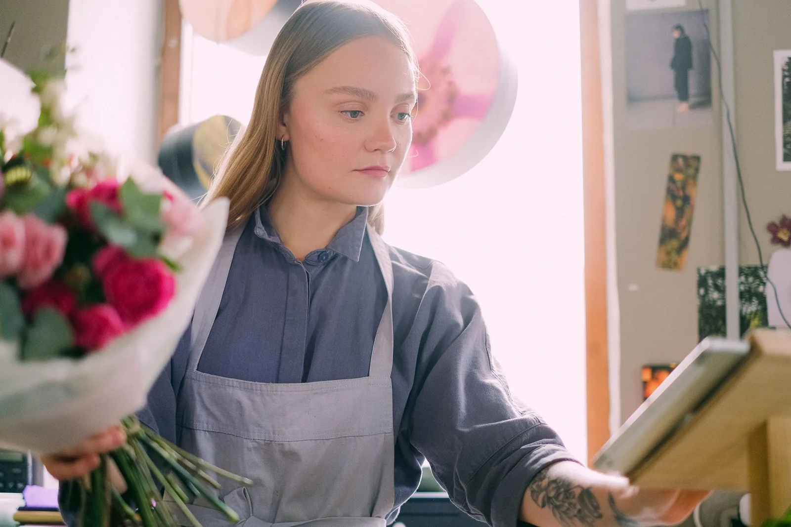 A florist in a grey apron holding a bouquet of pink and red roses at her workbench in a flower shop