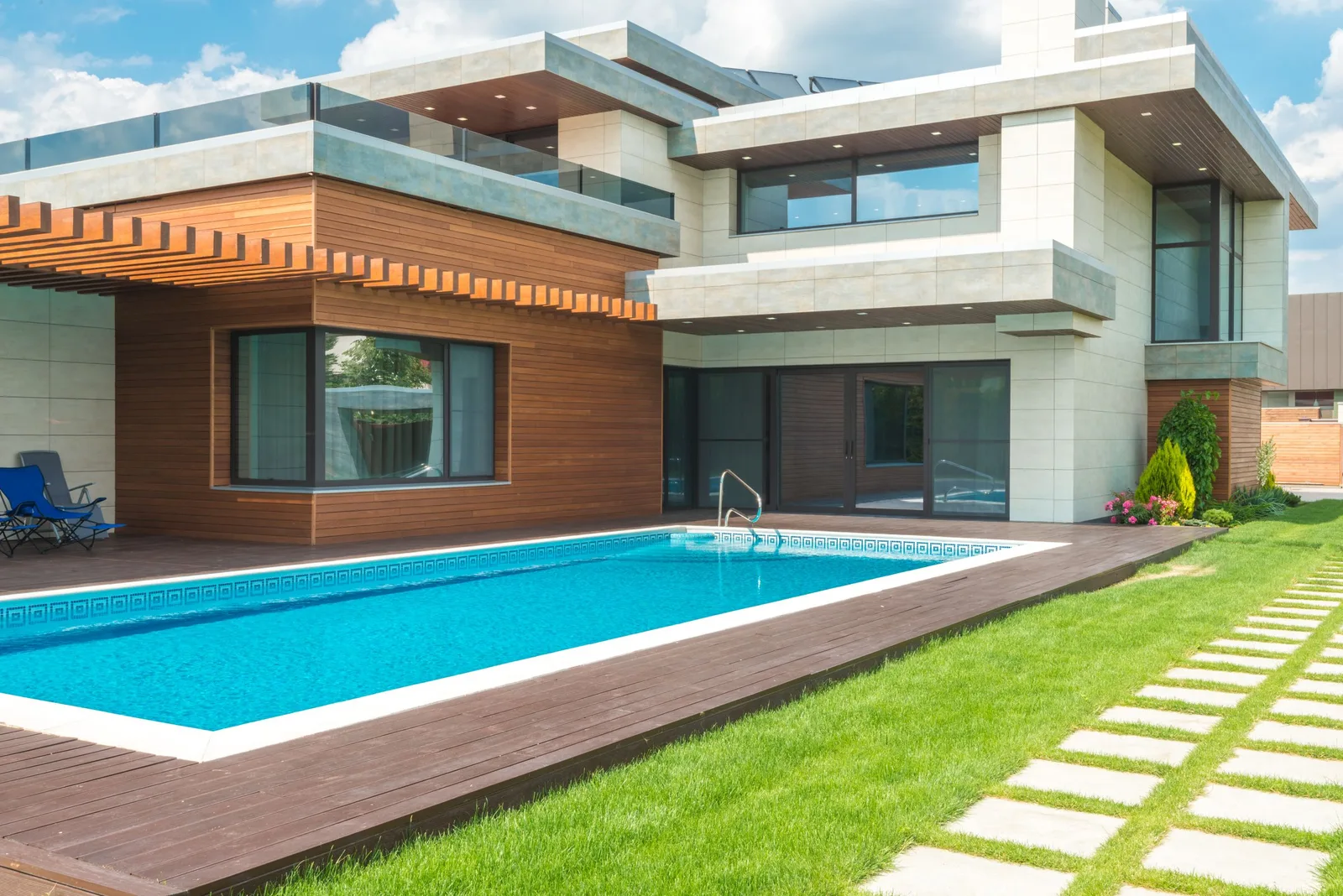 A modern two-storey house with a rectangular swimming pool, lawn and stepping stones in the back garden