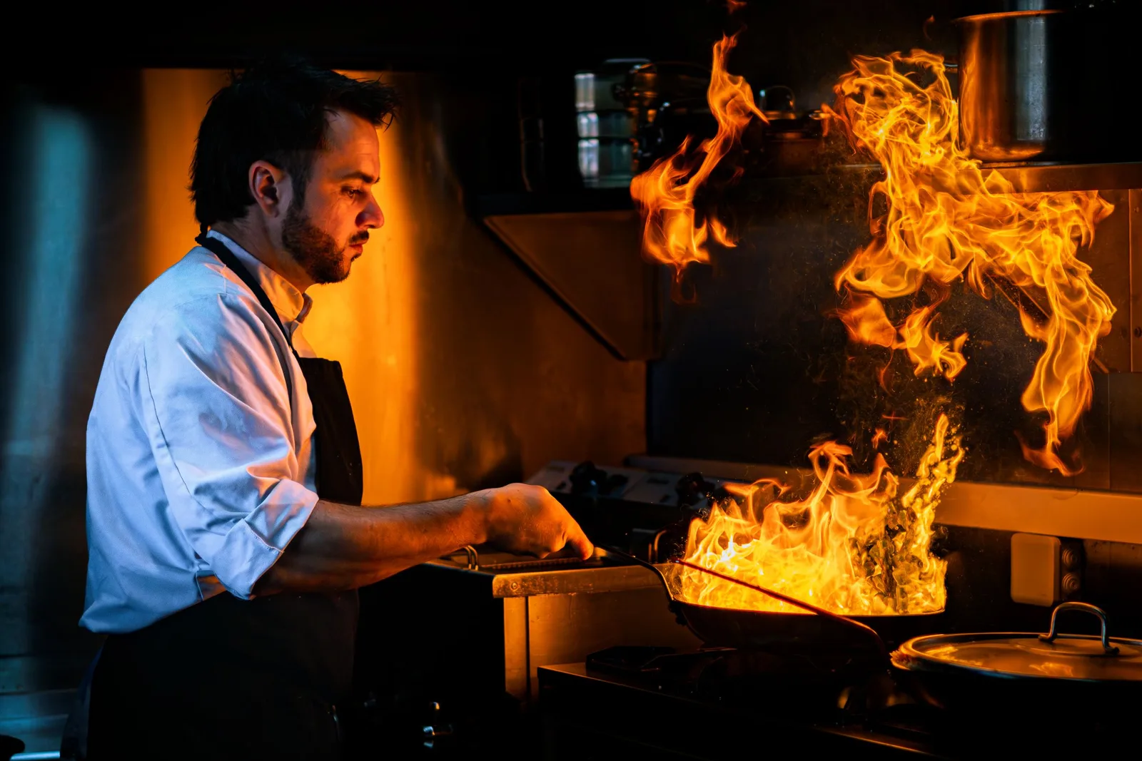 A chef cooking at a stove as a large flame rises from the pan