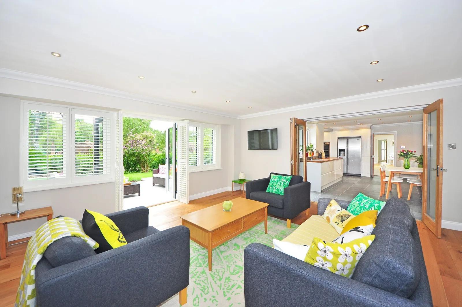 A bright open-plan living room with two grey sofas, a coffee table and a view through to the kitchen and garden
