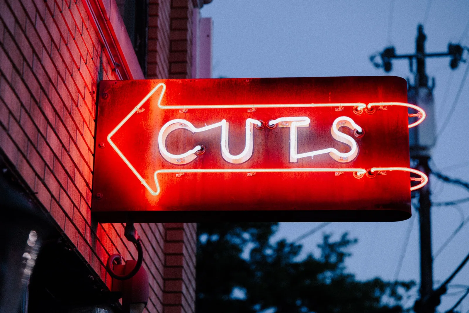A red neon sign reading CUTS on a brick wall